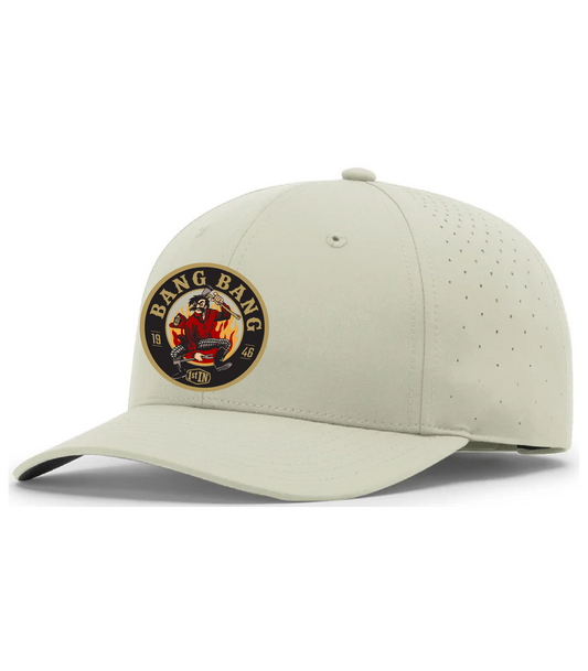 A light beige structured baseball cap with a curved brim, featuring a circular 'Bang Bang' woven patch on the front with a cartoon character holding fire fighters tools.