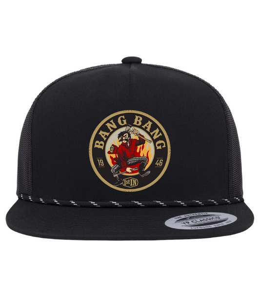 A black trucker hat with a circular woven embroidered 'Bang Bang' with a cartoon character holding fire fighter tools on the front panel. The hat has black mesh side panels, and a flat brim.