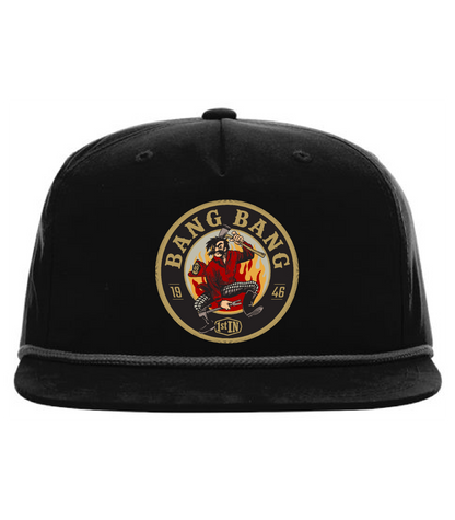 A black flat-brim baseball cap featuring a circular woven embroidered patch on the front with text that says 'BANG BANG' and a graphic of a cartoon character holding fire fighter tools.